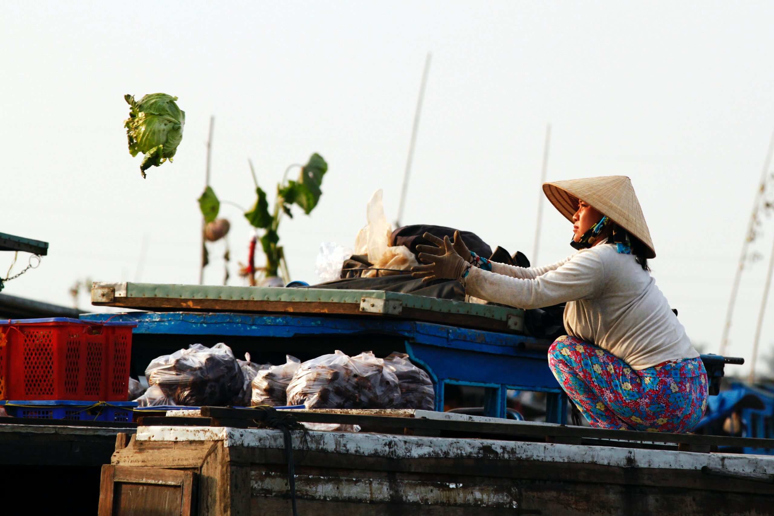 Mujer en un mercado flotante de Vietnam lanzando una lechuga.