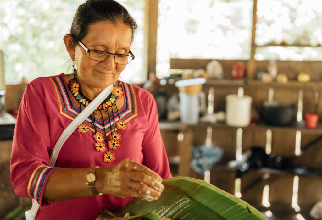 Mujer indígena kichwa preparando un almuerzo amazónico tradicional: maito de tilapia y palmito.